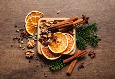 Photo of Different spices, dried orange slices and fir tree branches on wooden table, flat lay. Christmas season