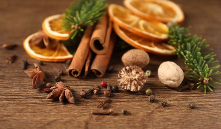 Photo of Different spices, dried orange slices and fir tree branches on wooden table, closeup. Christmas season