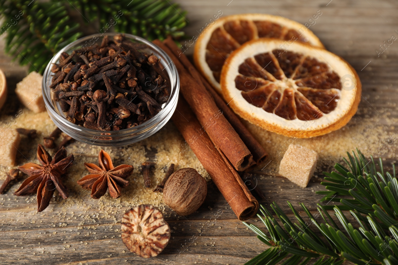 Photo of Different spices, dried orange slices and fir tree branches on wooden table, closeup. Christmas season