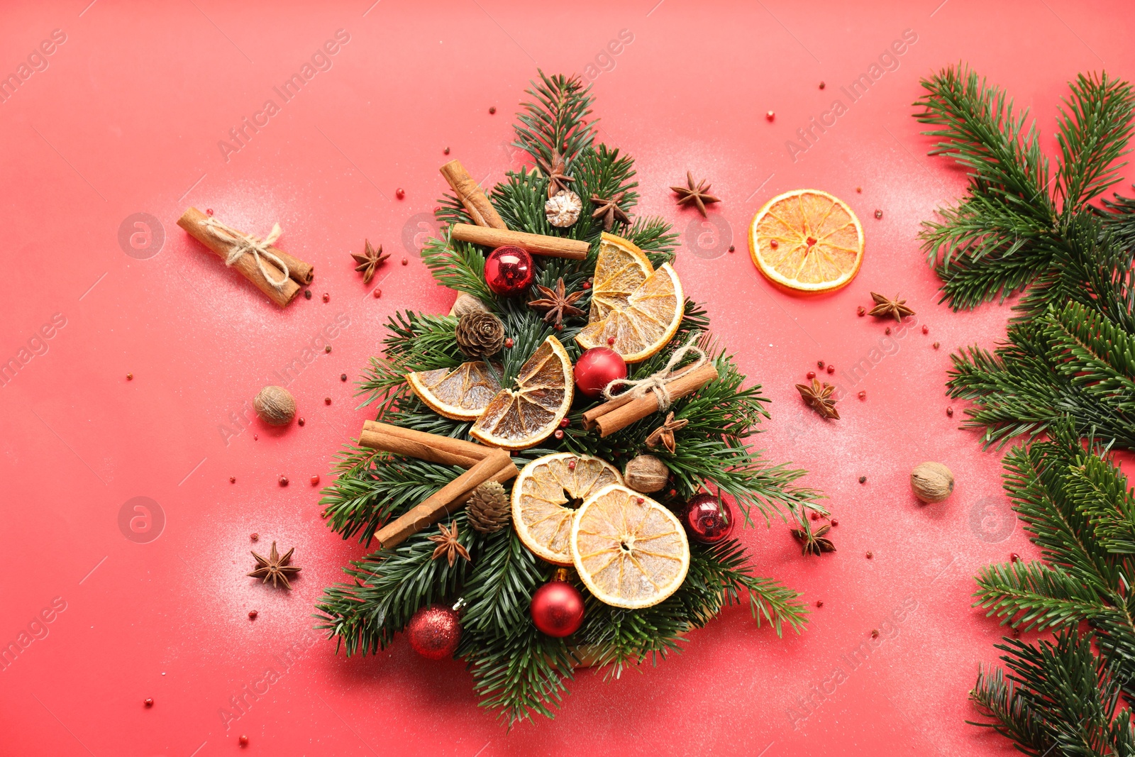 Photo of Christmas tree made of fir branches, baubles and different spices on red background, flat lay