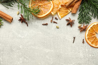 Photo of Different spices, dried orange slices and fir tree branches on light grey table, flat lay with space for text. Christmas season