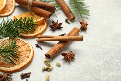 Photo of Different spices, dried orange slices and fir tree branches on light grey table, closeup with space for text. Christmas season