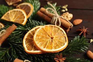 Photo of Different spices, dried orange slices and fir tree branches on wooden table, closeup. Christmas season