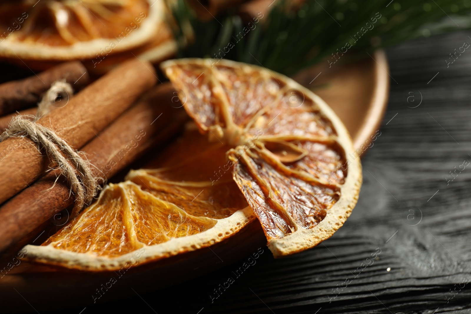 Photo of Different spices, dried orange slices and fir tree branches on black wooden table, closeup. Christmas season