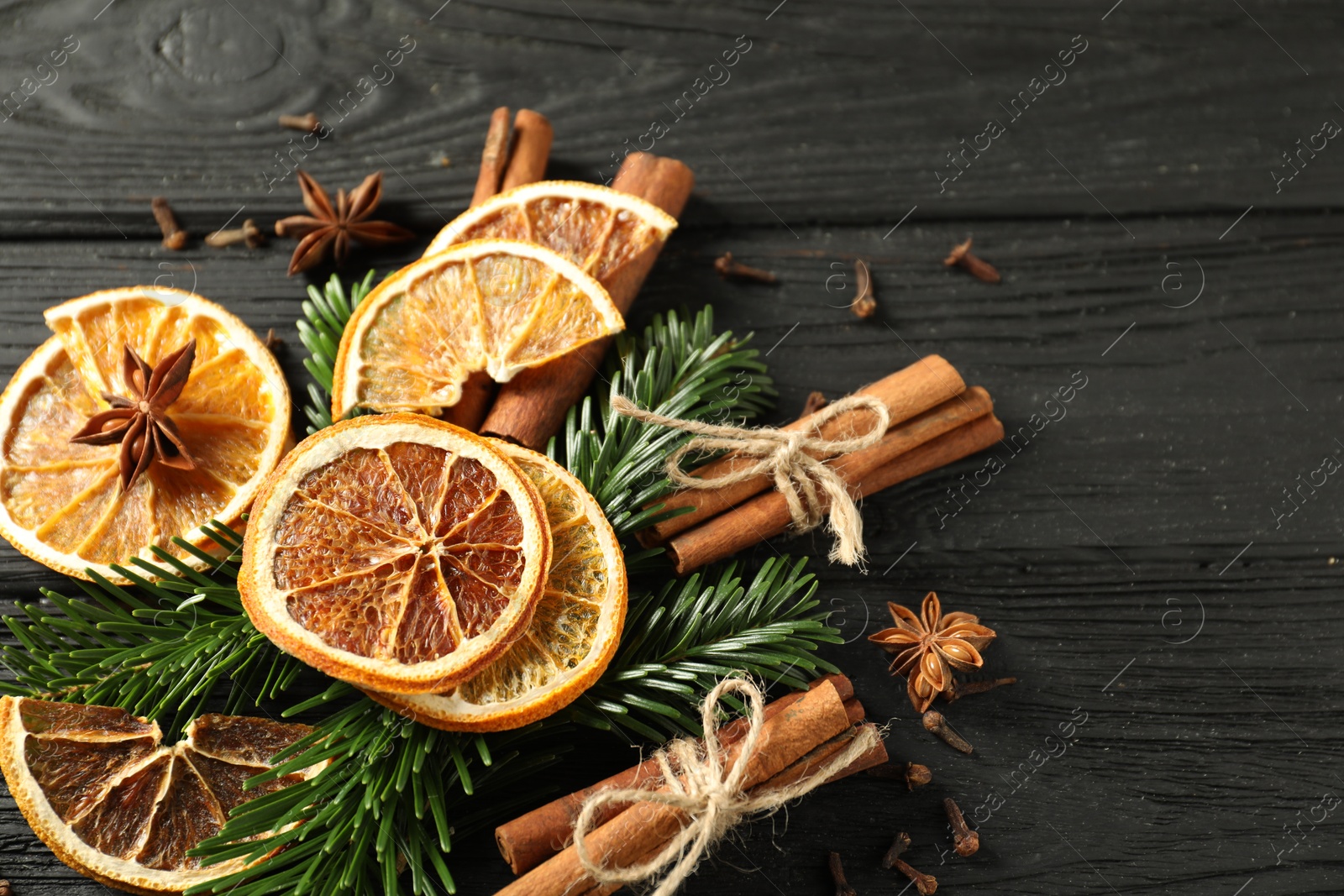 Photo of Different spices, dried orange slices and fir tree branches on black wooden table, above view with space for text. Christmas season