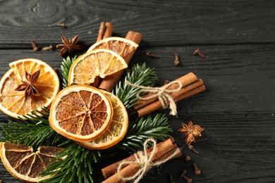 Photo of Different spices, dried orange slices and fir tree branches on black wooden table, above view with space for text. Christmas season