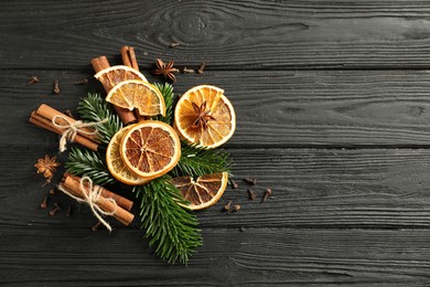 Photo of Different spices, dried orange slices and fir tree branches on black wooden table, flat lay with space for text. Christmas season