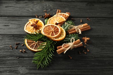 Photo of Different spices, dried orange slices and fir tree branches on black wooden table. Christmas season