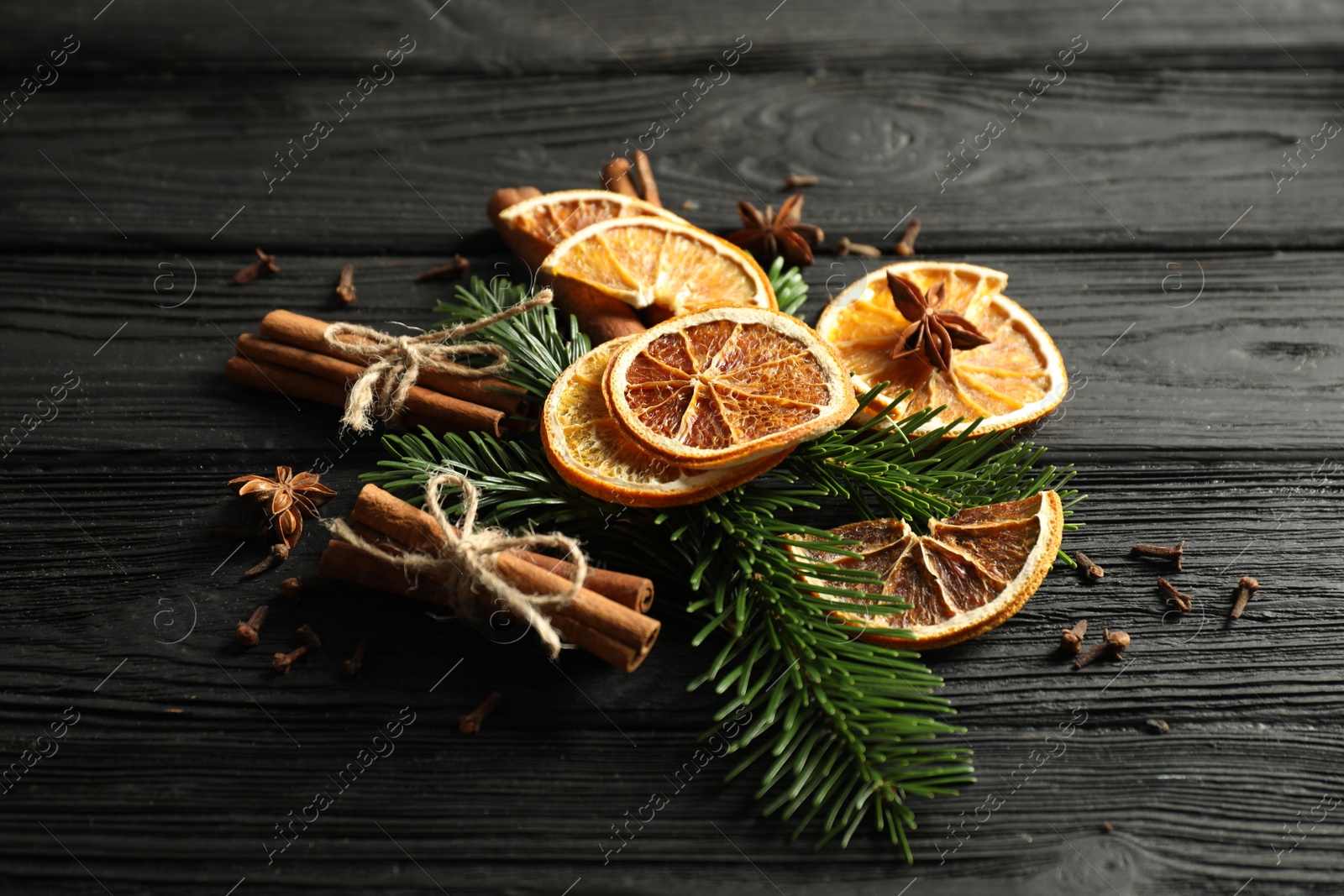 Photo of Different spices, dried orange slices and fir tree branches on black wooden table. Christmas season