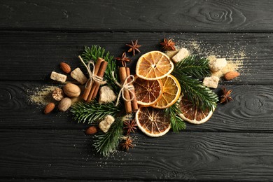 Photo of Different spices, dried orange slices and fir tree branches on black wooden table, flat lay. Christmas season