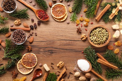 Photo of Frame of different aromatic spices and fir tree branches on wooden table, flat lay with space for text. Christmas season