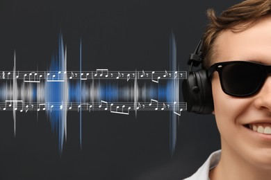 Image of Handsome young man with headphones on black background, closeup. Music notes and sound waves near him