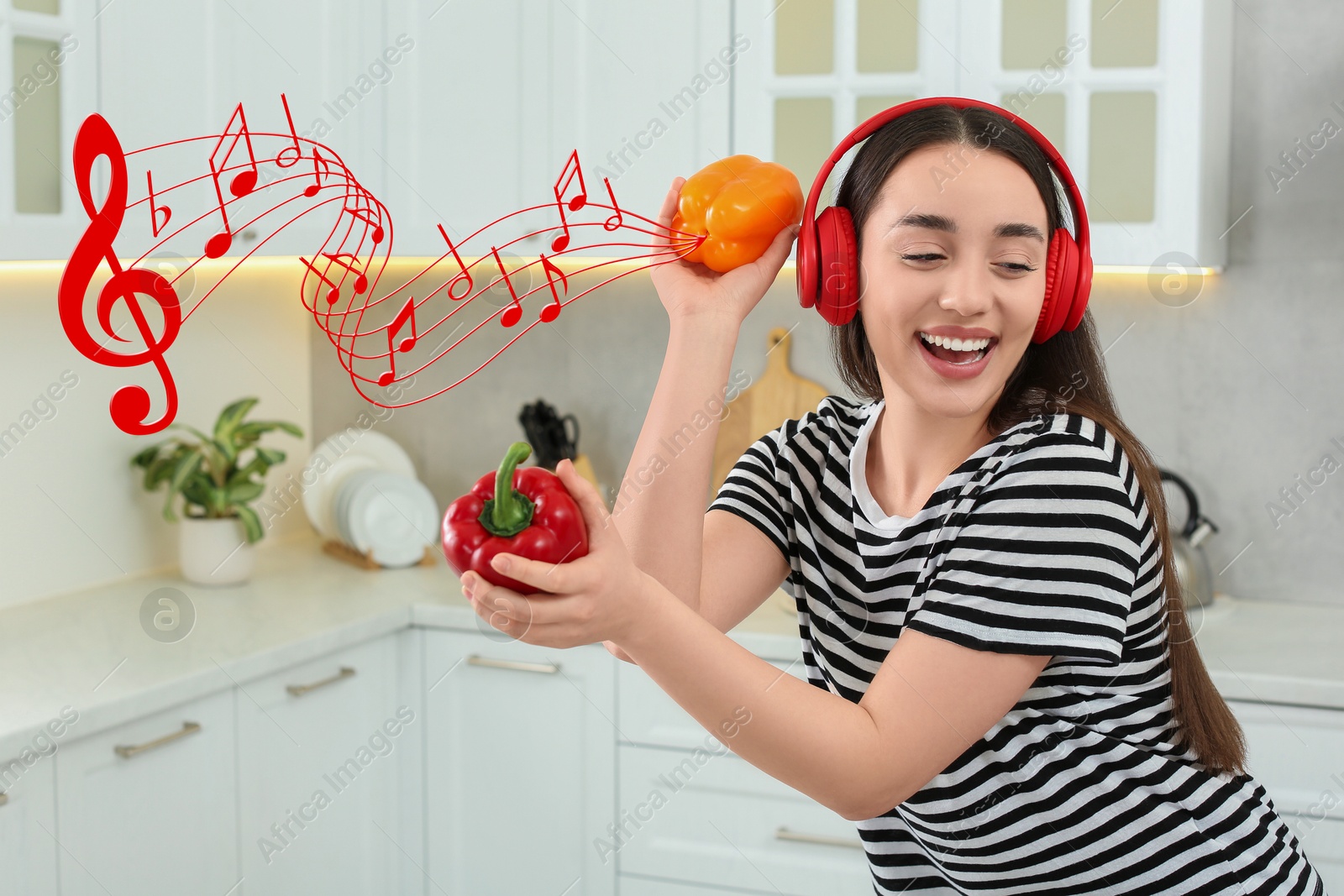 Image of Happy woman with headphones dancing with bell peppers in kitchen. Music notes flying near her