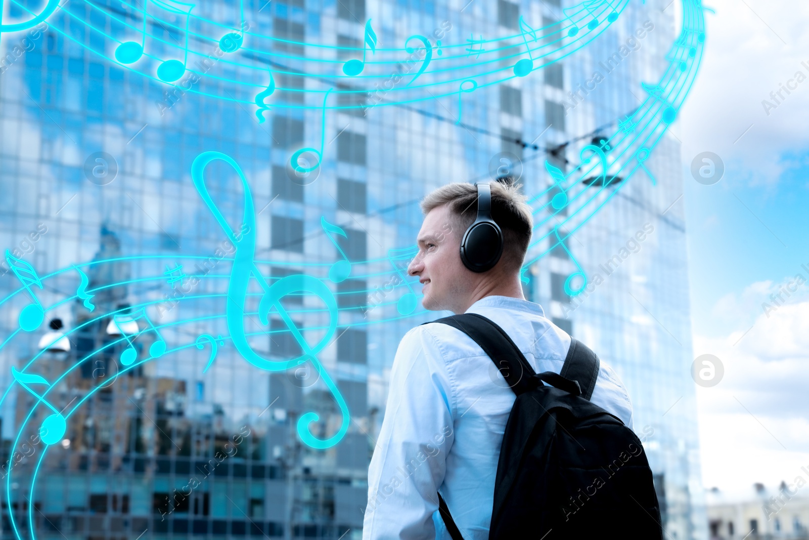 Image of Smiling man with headphones outdoors, back view. Music notes flying near him