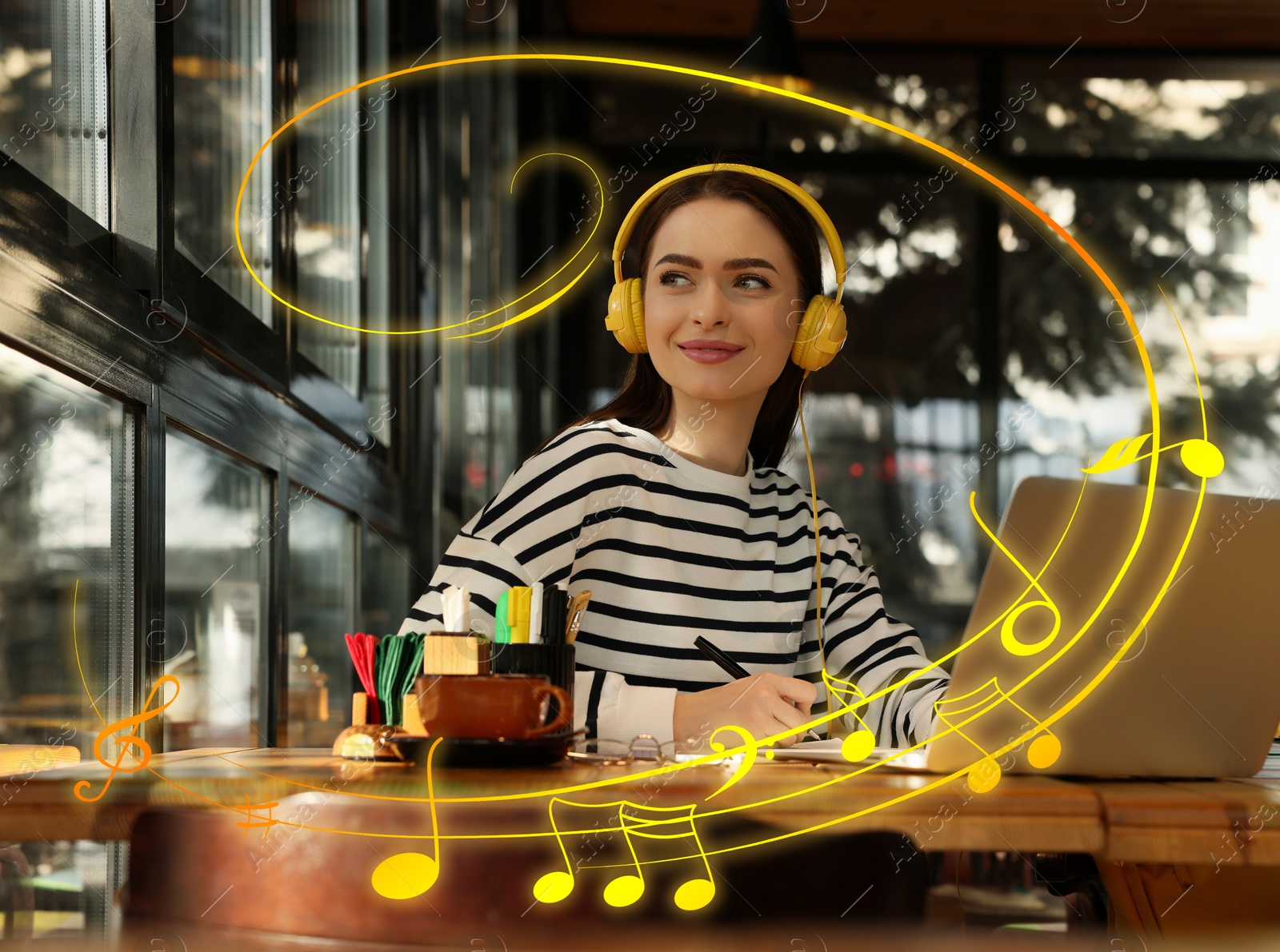 Image of Young student with laptop and headphones studying at table in cafe. Music notes flying near her