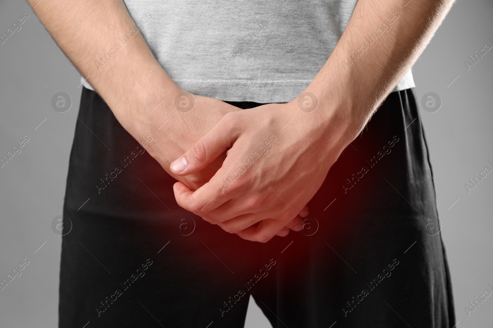 Image of STD (sexually transmitted diseases). Man holding hands near his groin on grey background, closeup