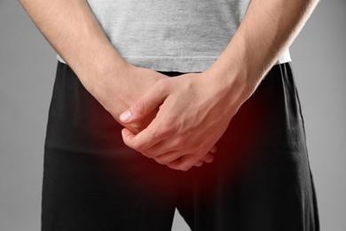 Image of STD (sexually transmitted diseases). Man holding hands near his groin on grey background, closeup