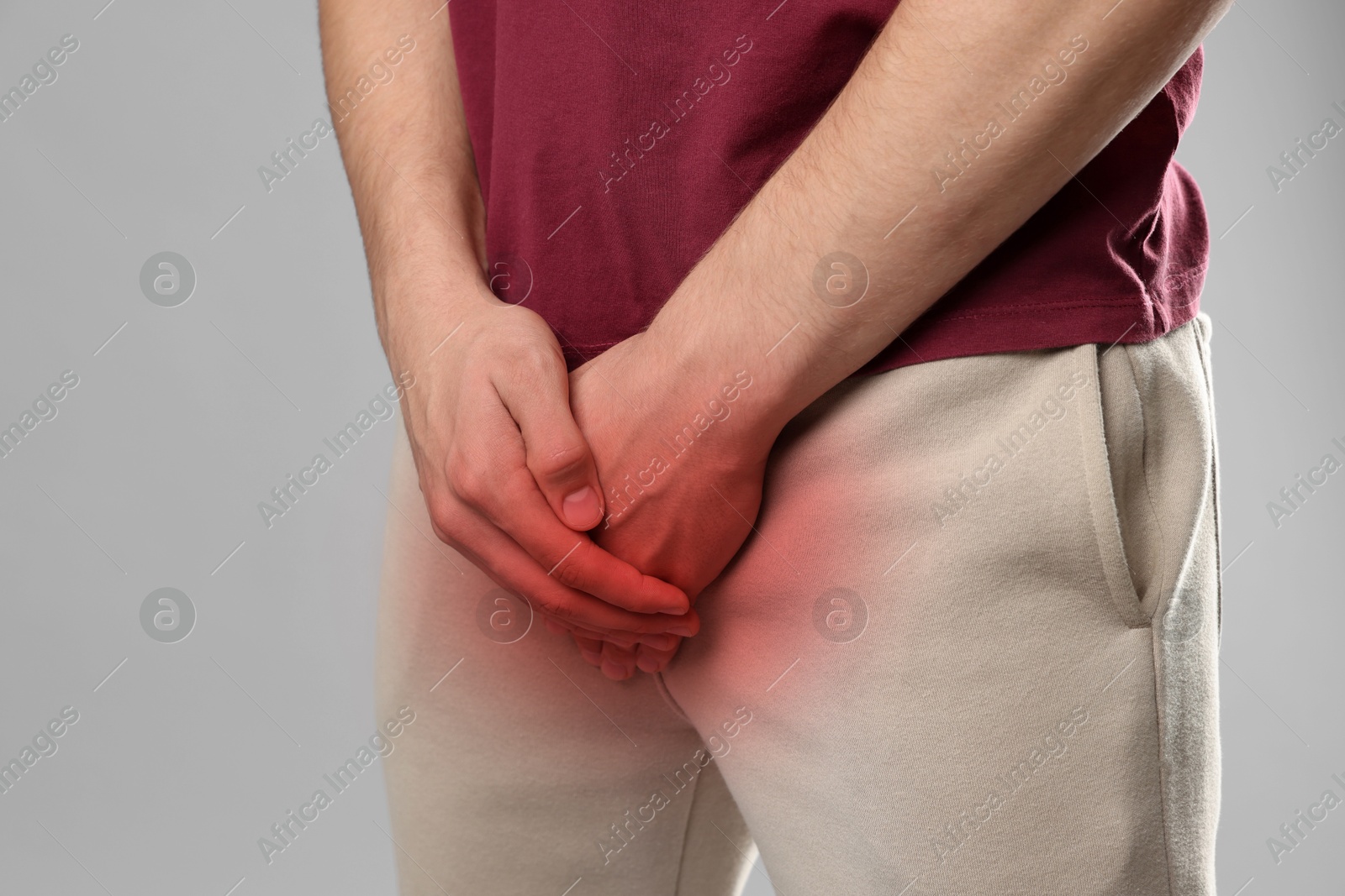 Image of STD (sexually transmitted diseases). Man holding hands near his groin on grey background, closeup