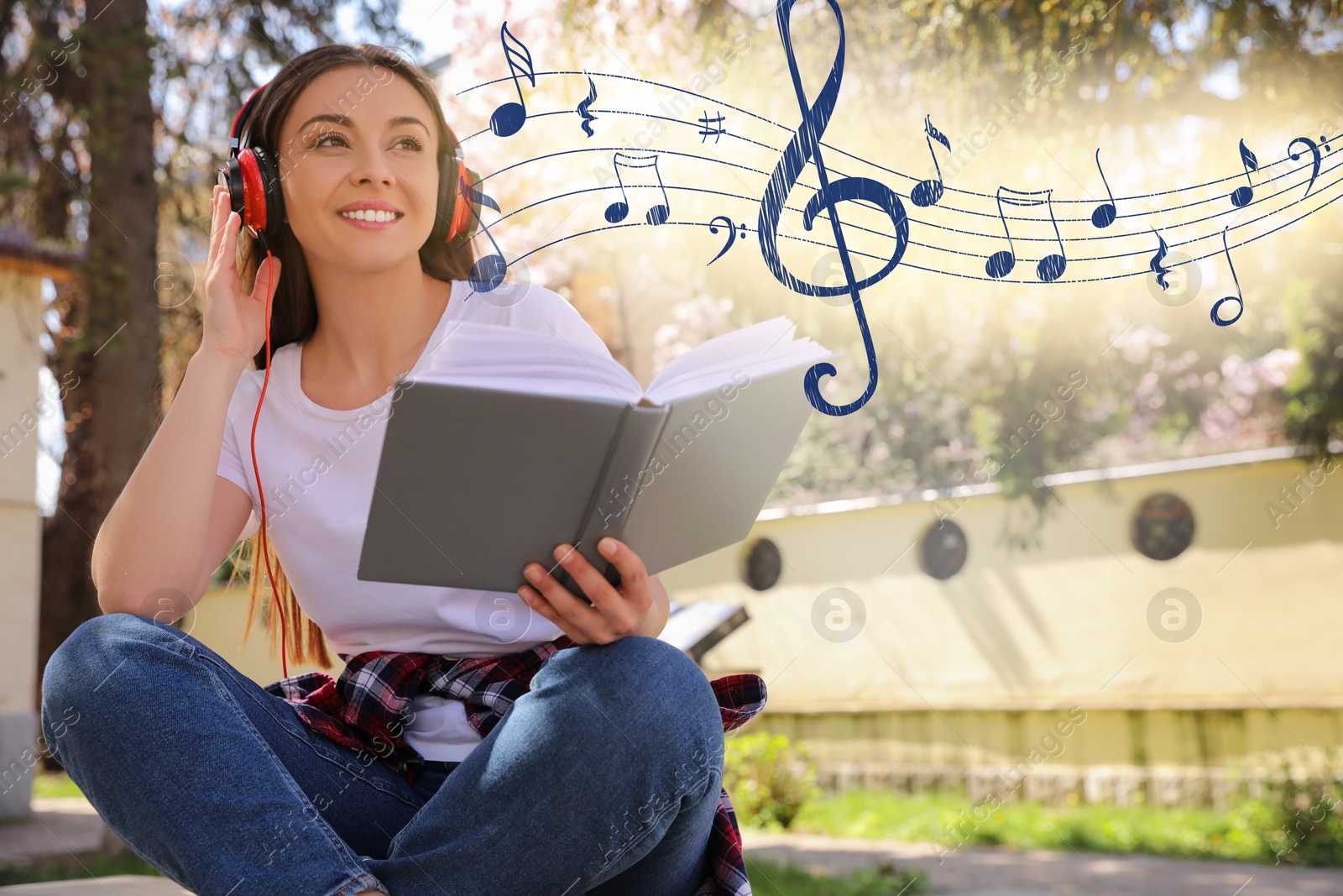 Image of Happy young woman with headphones reading book in park. Music notes flying near her