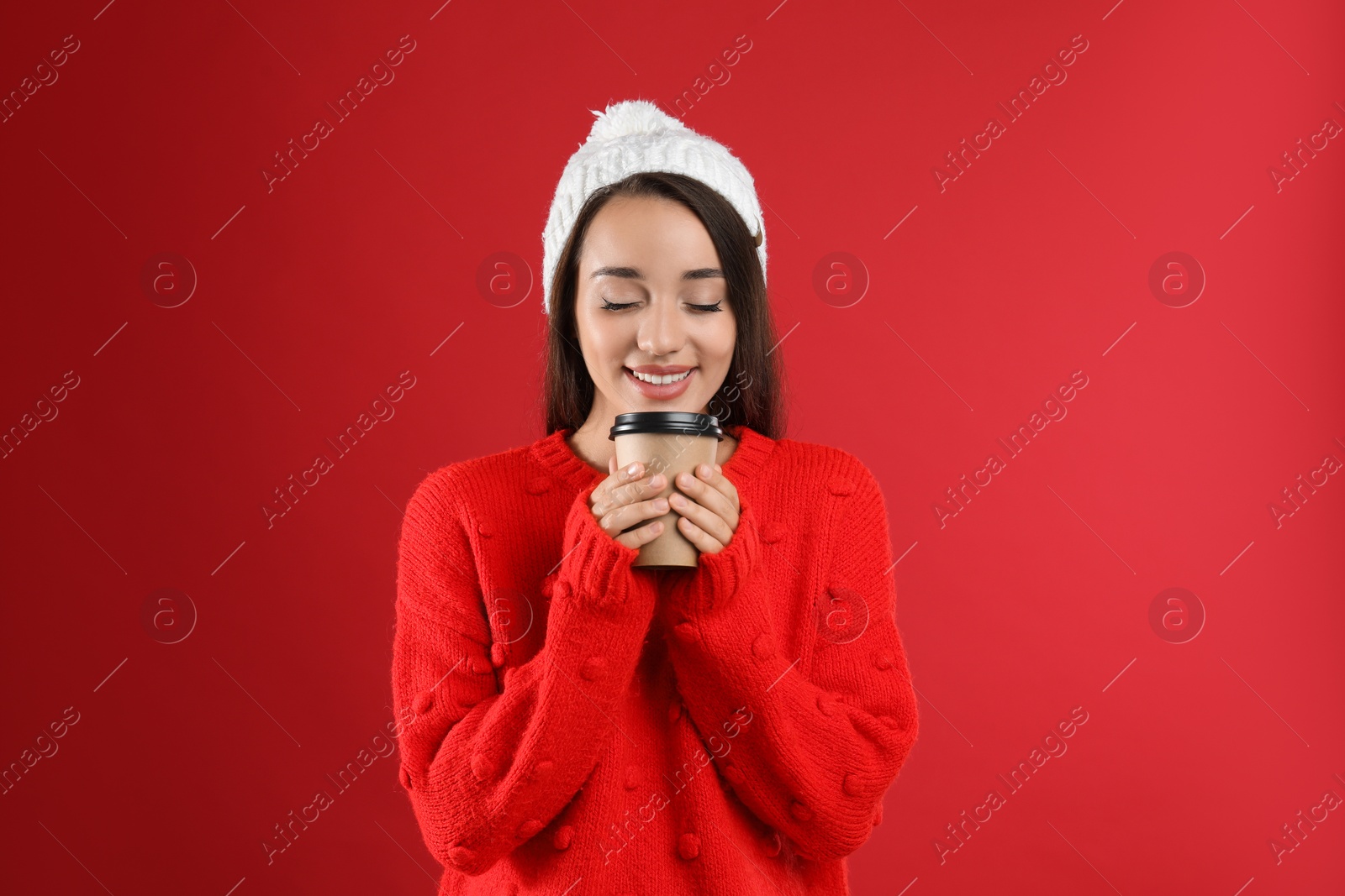 Photo of Happy beautiful woman with paper cup of mulled wine on red background