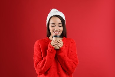 Photo of Happy beautiful woman with paper cup of mulled wine on red background