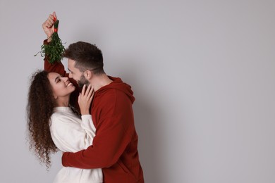 Photo of Lovely couple under mistletoe bunch on light grey background. Space for text