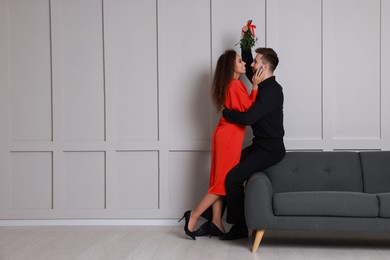 Photo of Lovely couple under mistletoe bunch near light grey wall indoors. Space for text