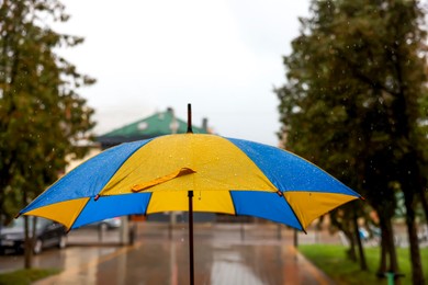 Photo of Yellow and blue umbrella outdoors on rainy day