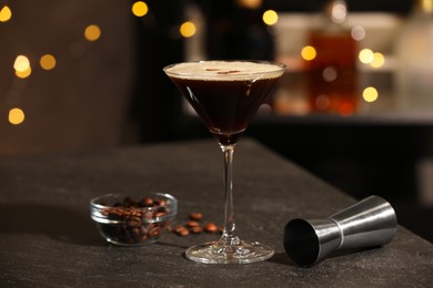 Photo of Glass with delicious espresso martini, coffee beans and jigger on table in bar