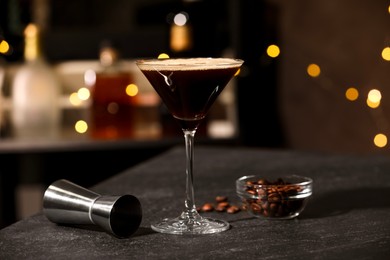 Photo of Glass with delicious espresso martini, coffee beans and jigger on table in bar