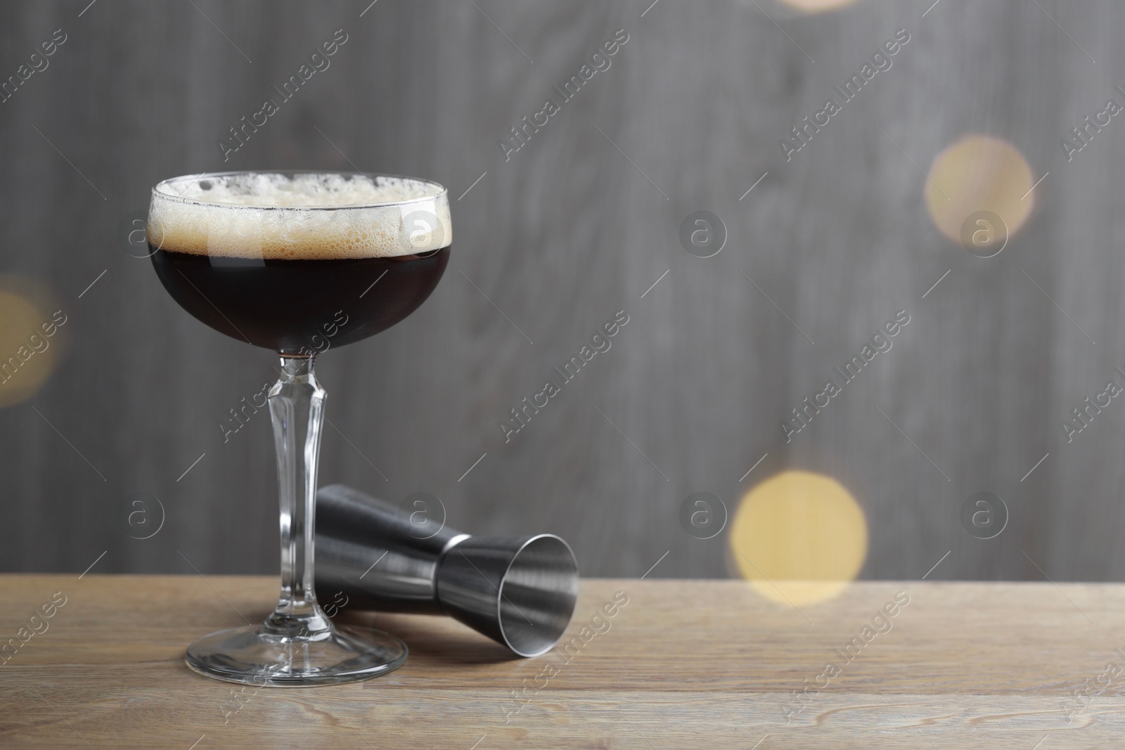 Photo of Delicious espresso martini with coffee beans in glass and jigger on wooden table. Space for text