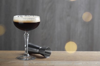 Photo of Delicious espresso martini with coffee beans in glass and jigger on wooden table. Space for text