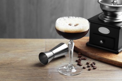 Photo of Delicious espresso martini in glass, coffee beans, manual grinder and jigger on wooden table. Space for text