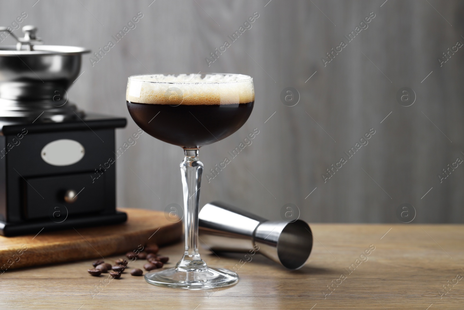 Photo of Delicious espresso martini in glass, coffee beans, manual grinder and jigger on wooden table. Space for text