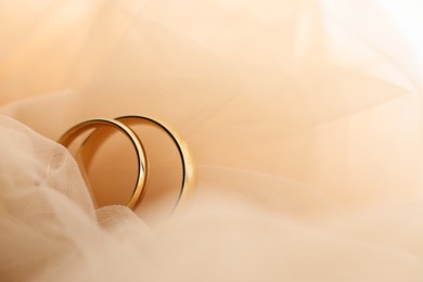 Photo of Beautiful golden wedding rings on beige fabric, closeup. Space for text