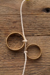 Photo of Beautiful golden wedding rings tied with thread on wooden background, top view