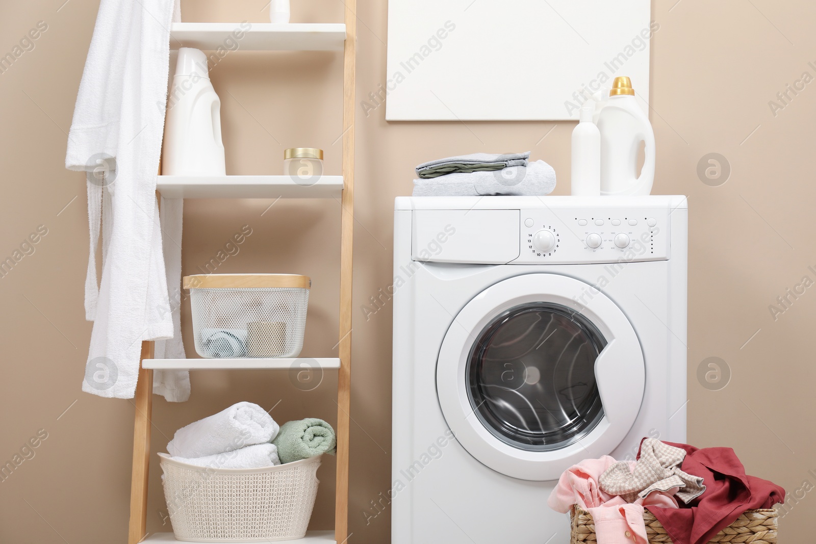 Photo of Laundry detergents, clothes, washing machine and decorative ladder in bathroom