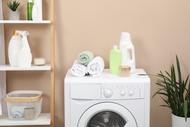 Photo of Laundry detergents, terry towels, washing machine and decorative ladder in bathroom