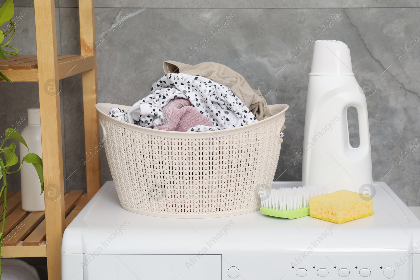 Photo of Detergent, brush, sponge and basket with laundry on washing machine indoors