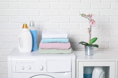 Photo of Laundry detergents and stacked clean towels on washing machine in bathroom