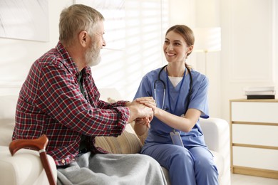 Caregiver supporting senior man on sofa. Home health care service