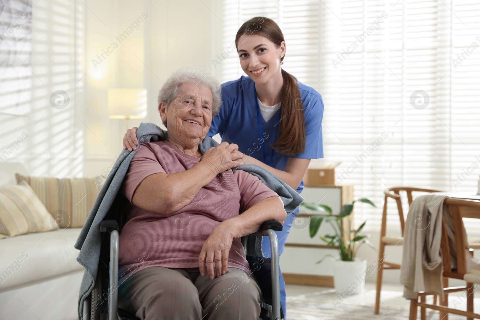 Photo of Caregiver covering senior woman with blanket indoors. Home health care service