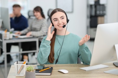 Photo of Saleswoman talking to client via headset at desk in office