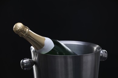 Photo of Bottle of champagne in bucket on black background, closeup