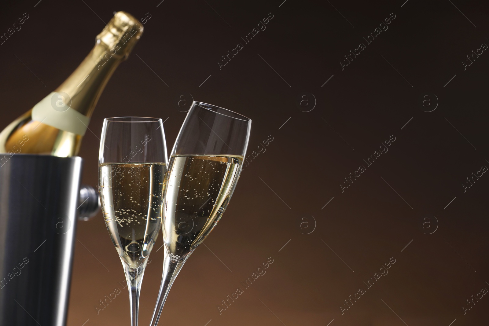 Photo of Champagne in glasses and ice bucket with bottle on brown background, space for text