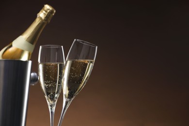 Photo of Champagne in glasses and ice bucket with bottle on brown background, space for text