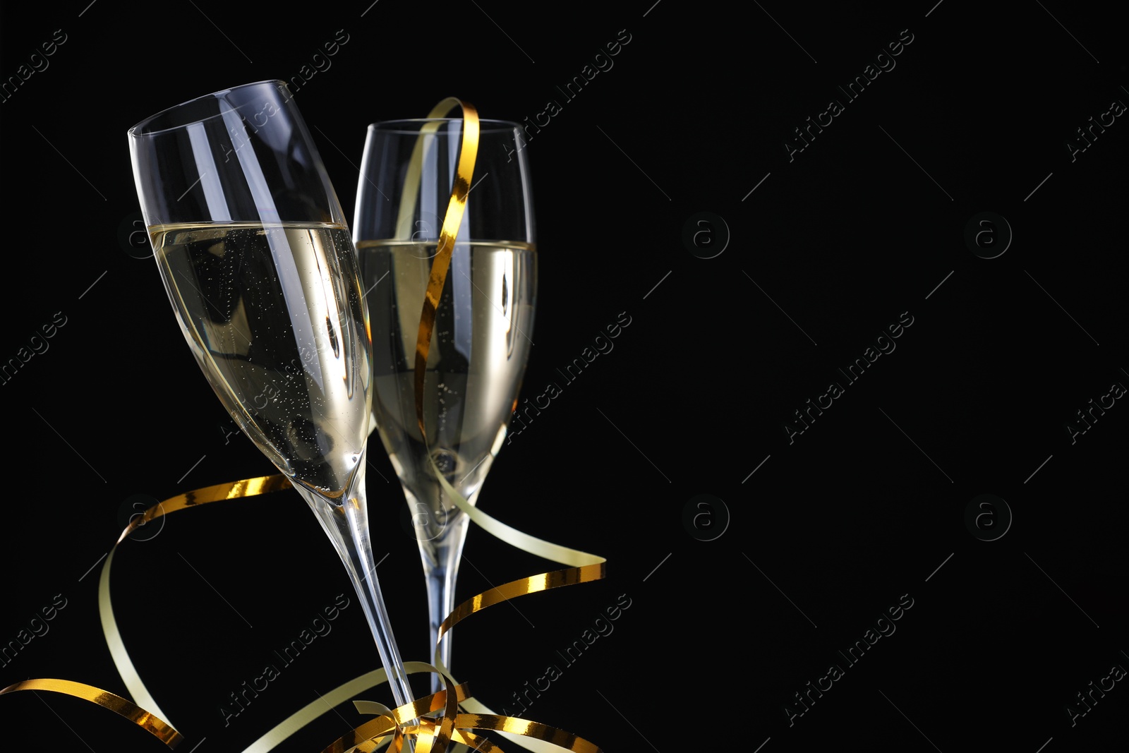 Photo of Champagne in glasses and party streamers on black background, space for text