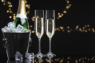 Photo of Champagne and bucket of ice on mirror surface against black background with blurred lights, space for text