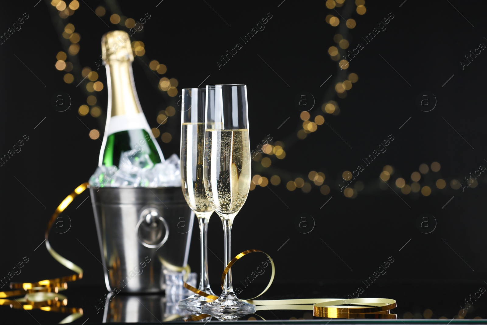 Photo of Champagne and bucket of ice on mirror surface against black background with blurred lights, space for text