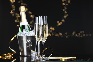 Photo of Champagne and bucket of ice on mirror surface against black background with blurred lights, space for text